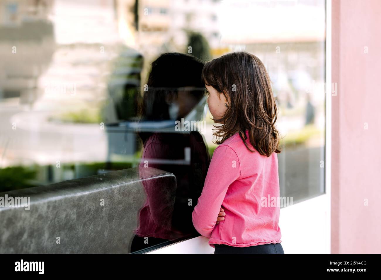 Seitenansicht eines ernsthaften Mädchens in legerer Kleidung, das auf das Glasfenster des modernen Salons blickt, während es auf der Straße der Stadt steht Stockfoto
