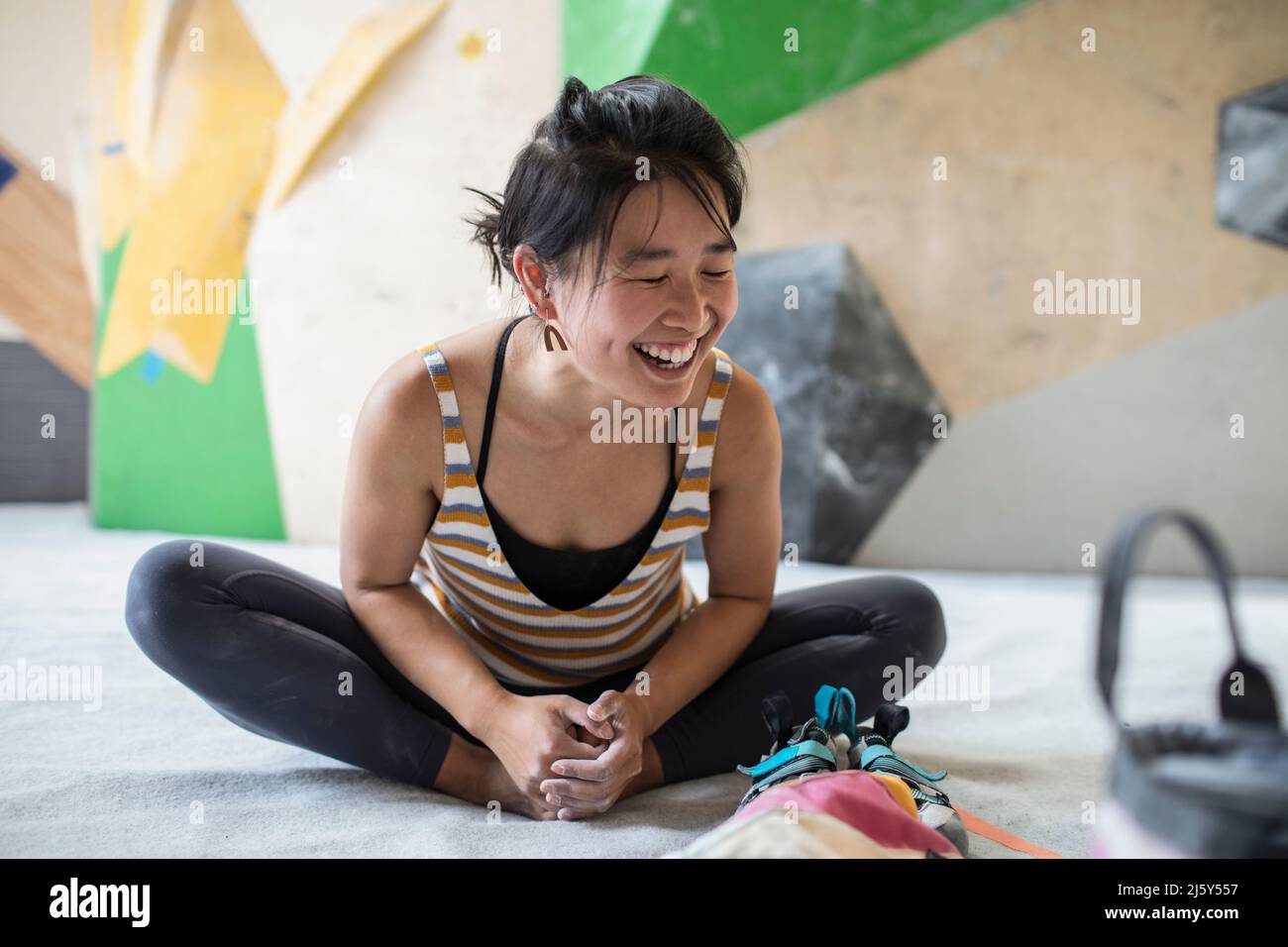 Glückliche weibliche Klettererin, die sich in der Kletterhalle dehnt Stockfoto