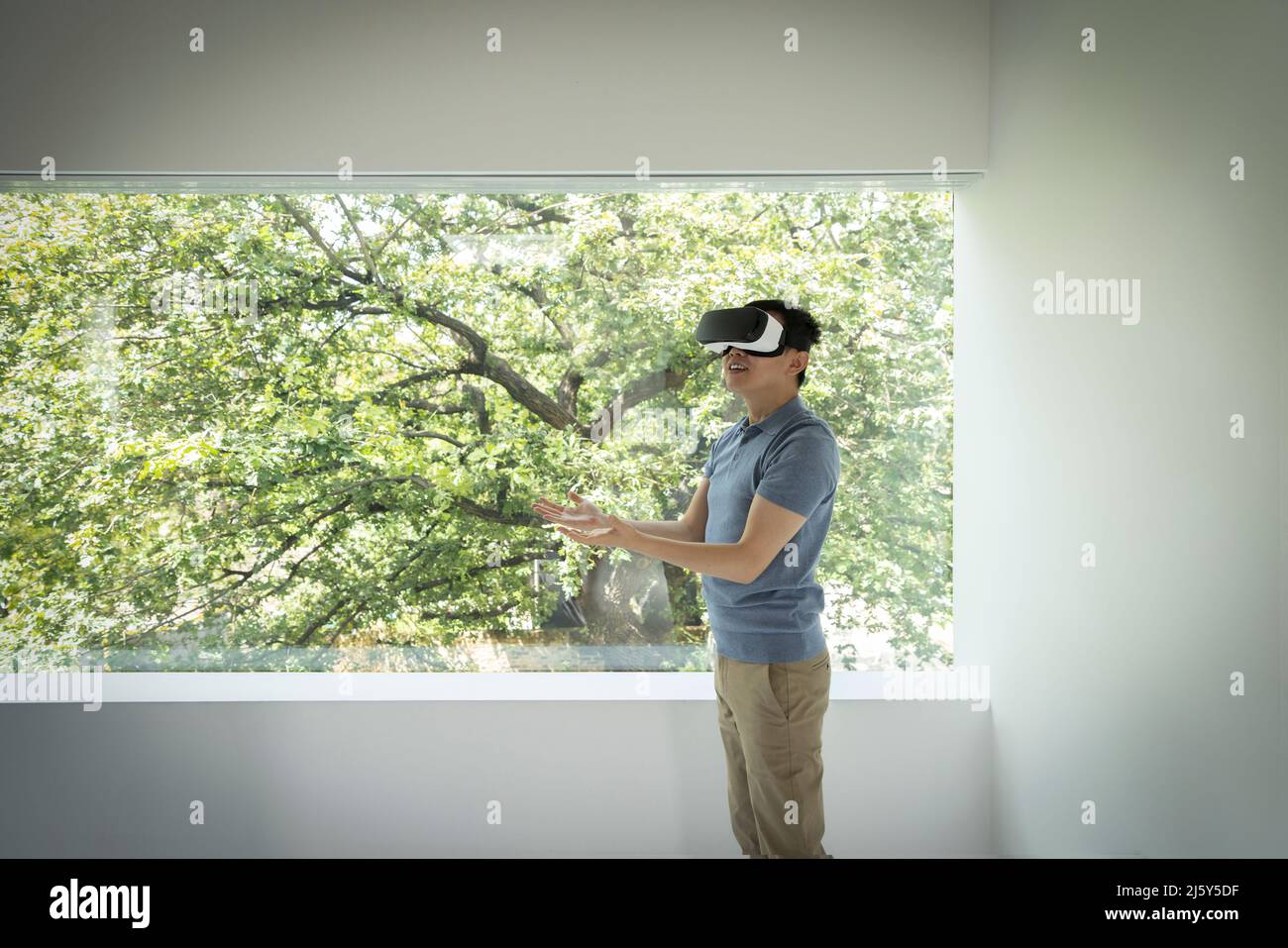 Mann mit VR-Headset am Fenster mit Blick auf den Baum Stockfoto