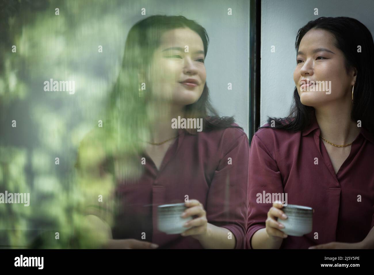 Nachdenkliche junge Frau, die am Fenster Tee trinkt Stockfoto