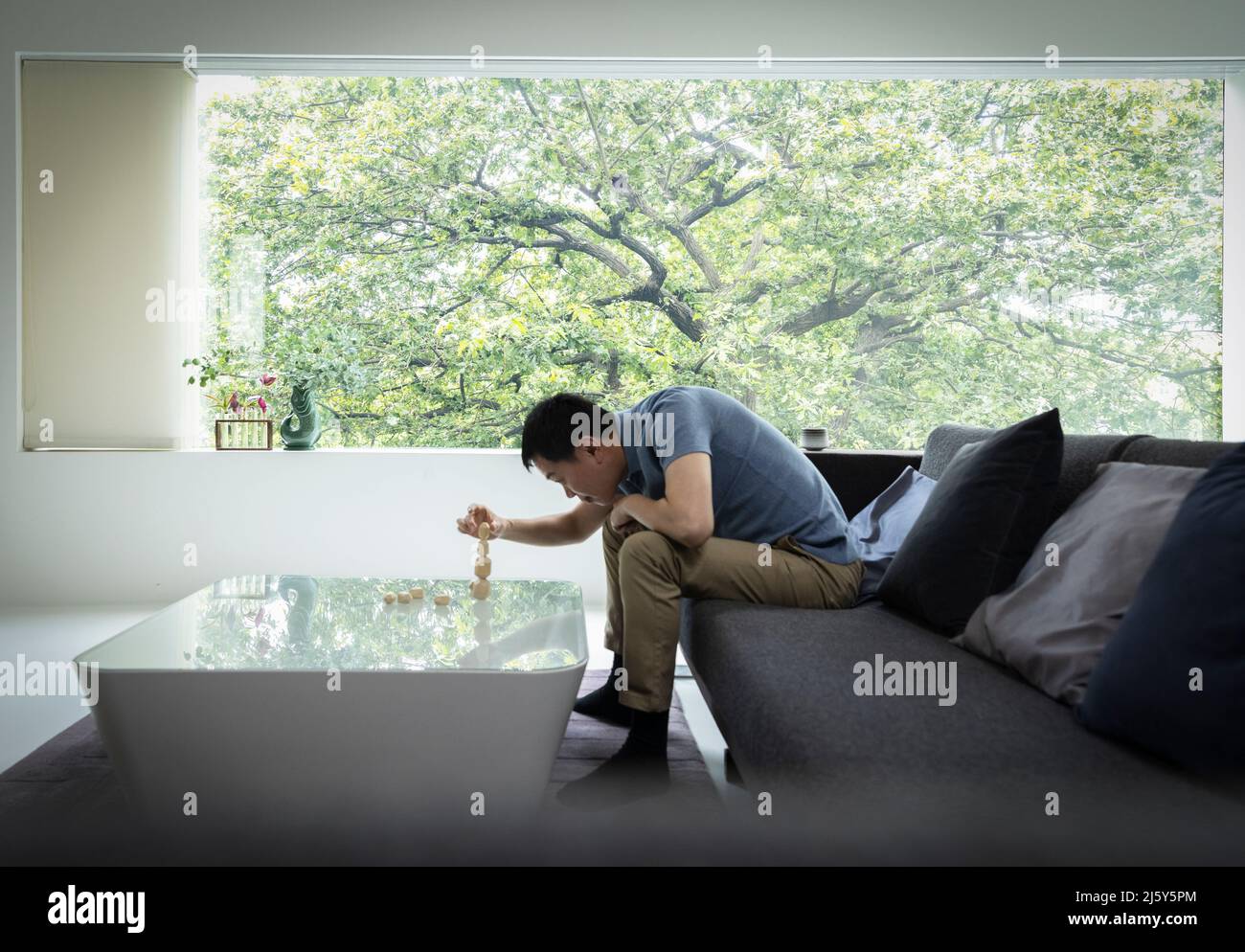 Mann stapelt Steine auf Couchtisch im modernen Wohnzimmer Stockfoto