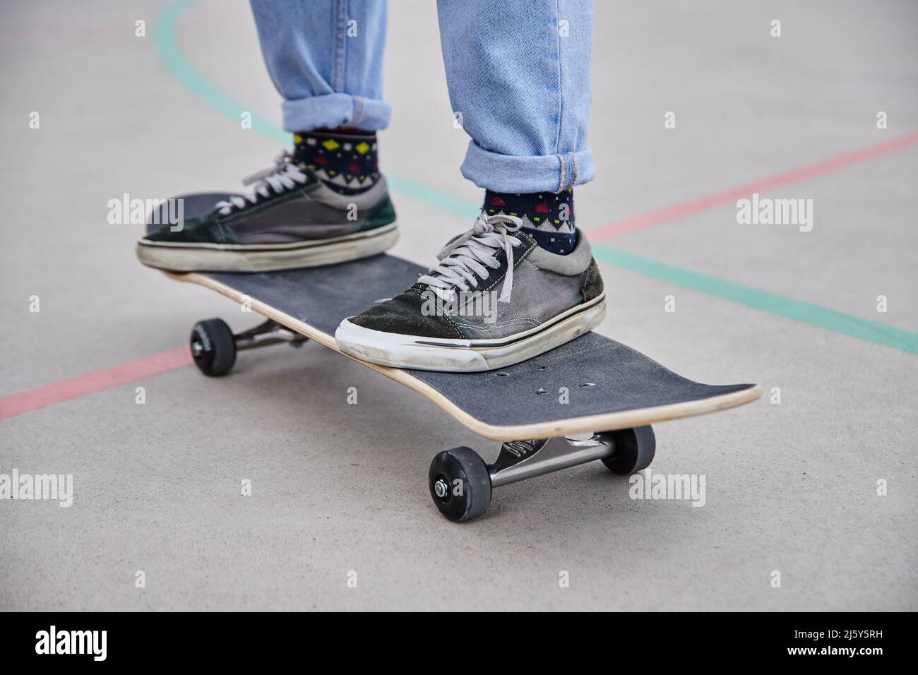 Cropped unkenntlich aktive schnelle Person in Freizeitkleidung Reiten Skateboard auf Sportplatz in der Nähe von hohen Bäumen am Sommertag Stockfoto