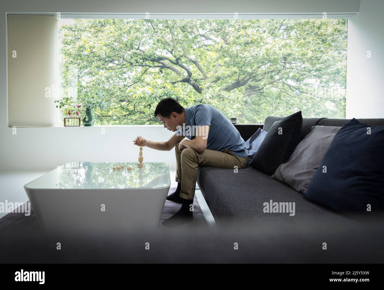 Mann stapelt Steine auf einem modernen Couchtisch im Wohnzimmer Stockfoto
