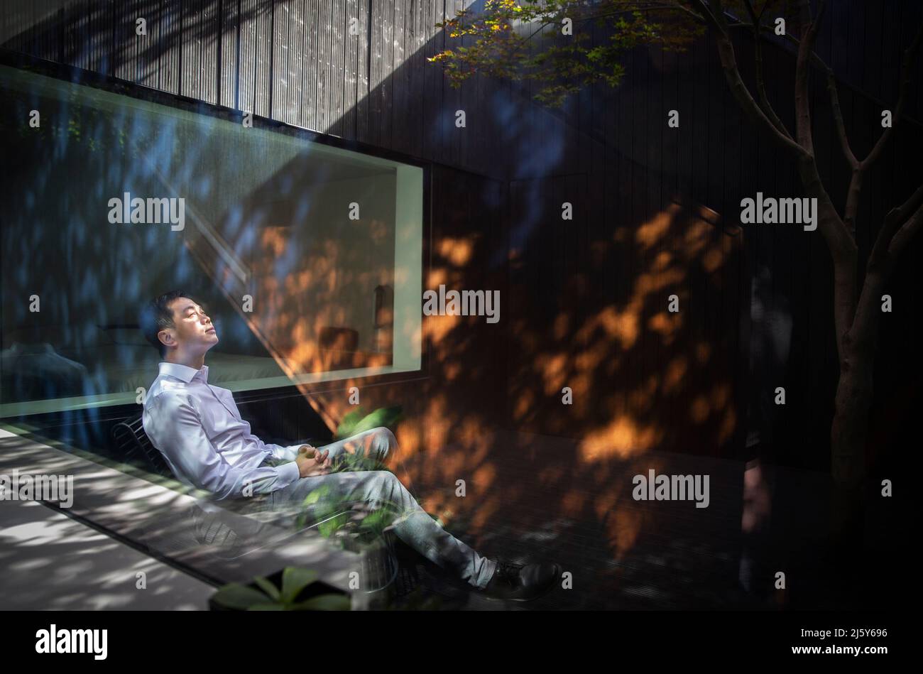 Ruhiger Mann, der im Innenhof im Sonnenlicht sitzt Stockfoto