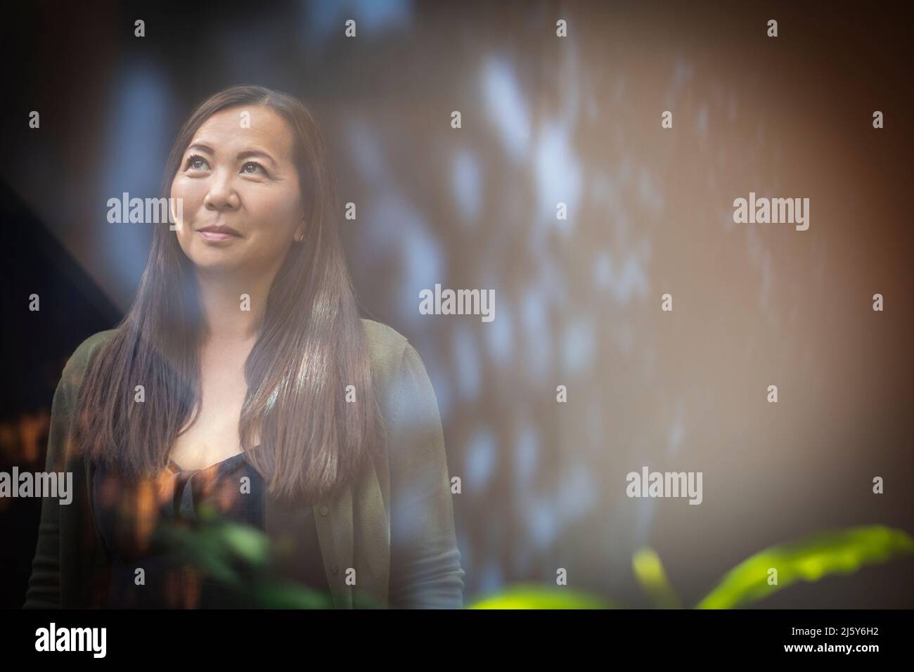 Lächelnde Frau, die mit Reflexionen zum Fenster aufblickt Stockfoto