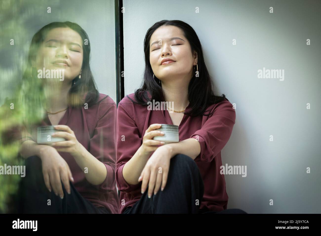 Ruhige junge Frau, die im Fenster Tee trinkt Stockfoto