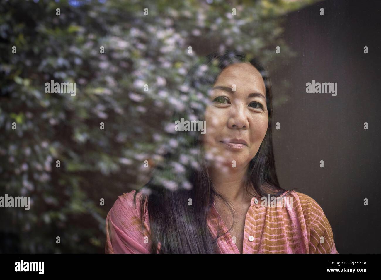 Portrait selbstbewusste Frau am Fenster mit Spiegelung des Baumes Stockfoto