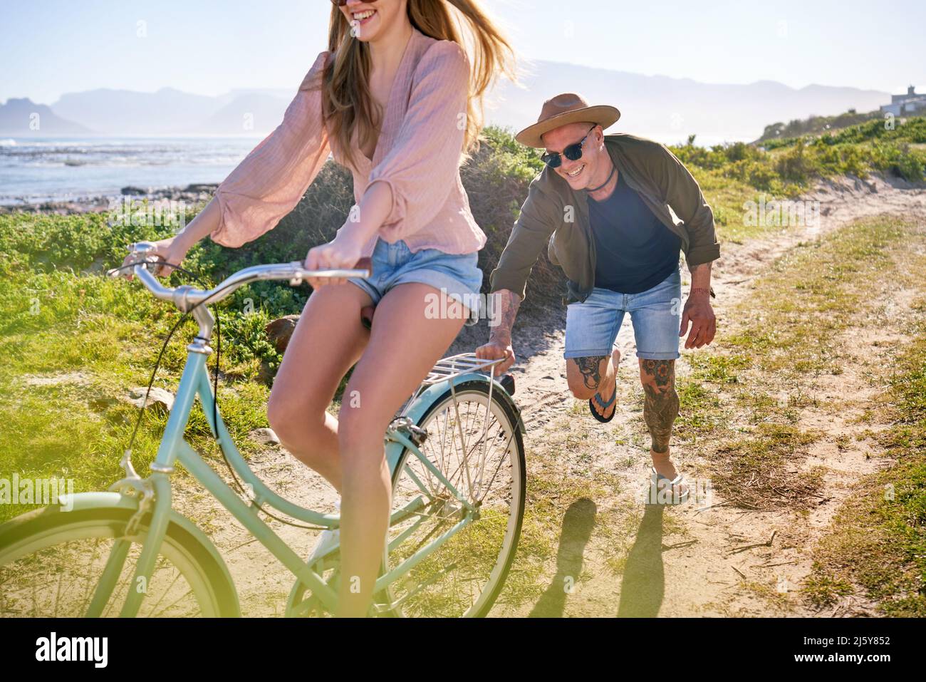 Happy Boyfriend schiebt Freundin auf Fahrrad auf sonnigen Strandweg Stockfoto