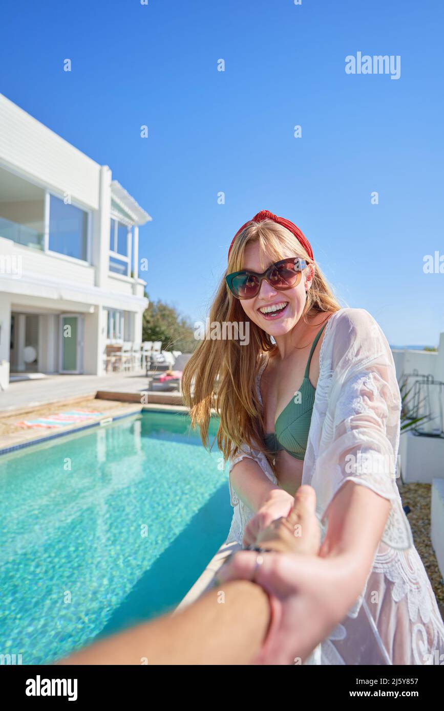 POV glücklich junge Frau zieht Freund am sonnigen Schwimmbad Stockfoto