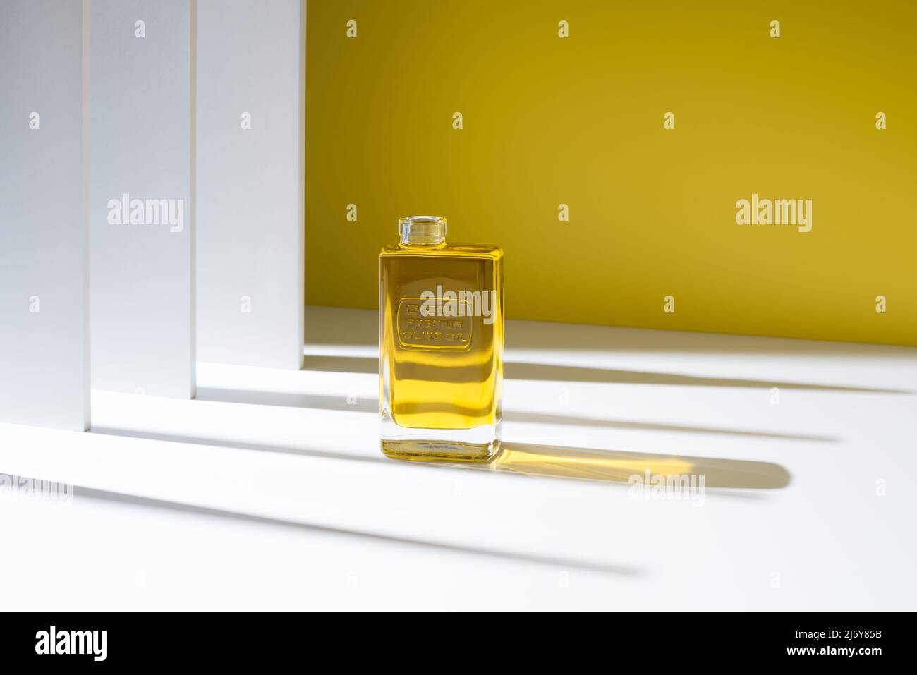 Transparente Glasflasche mit teuren natürlichen Olivenöl von Premium-Qualität in minimalistischen stilvollen Studio gegen gelbe Wand platziert Stockfoto