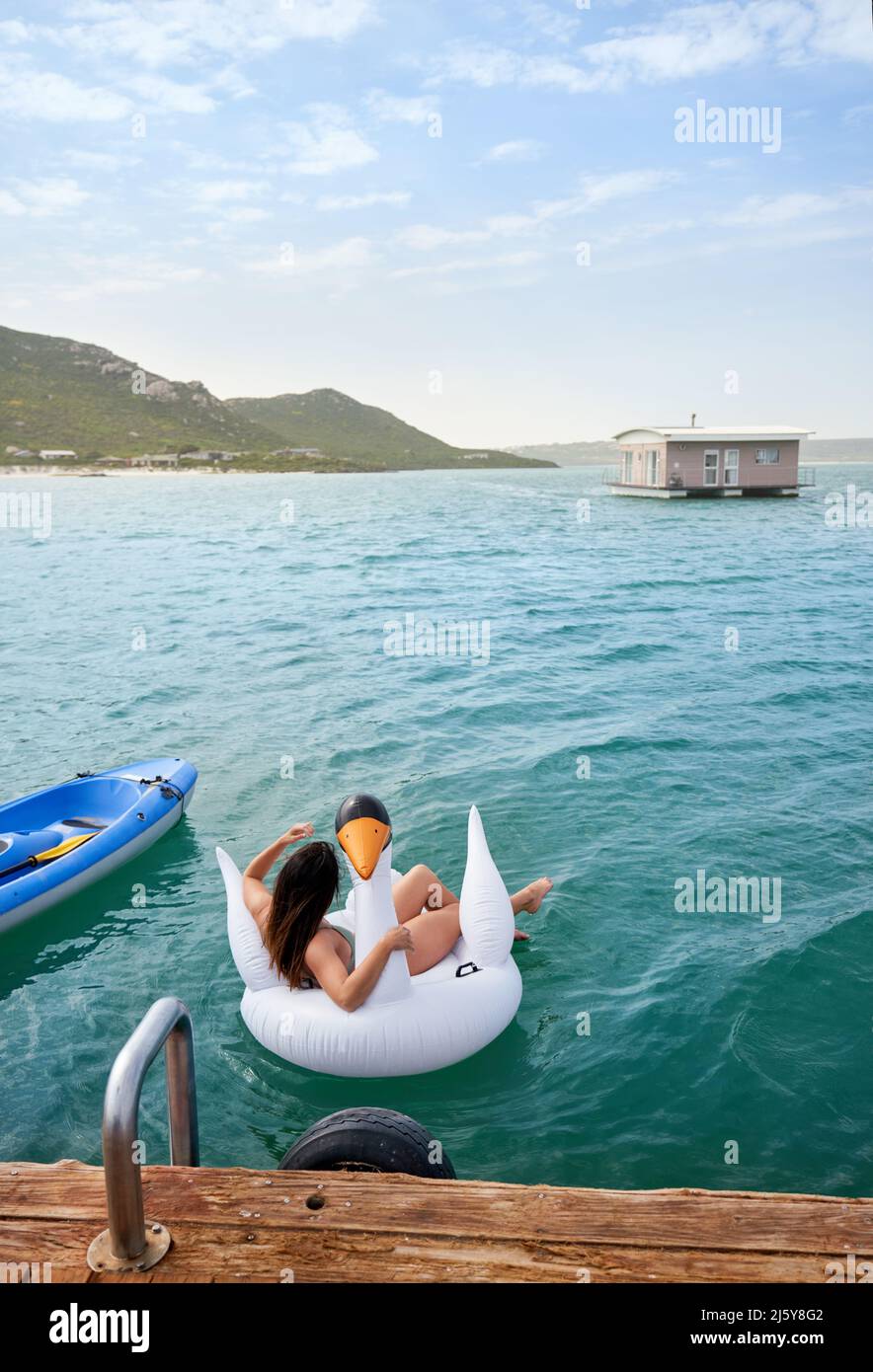 Frau, die sich auf einem aufblasbaren Schwan im blauen Ozean entspannt Stockfoto