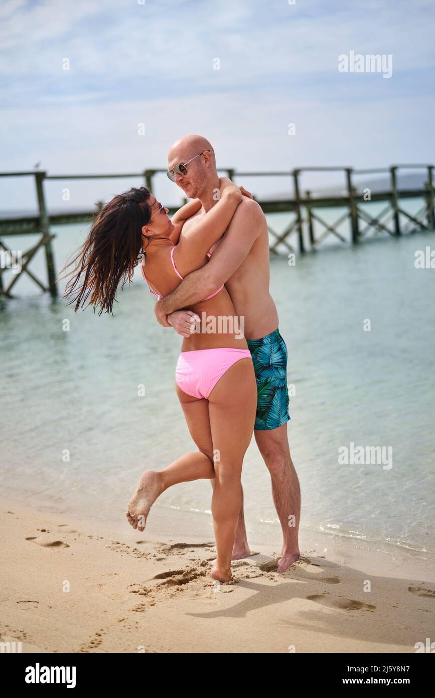 Glückliches, liebevolles Paar, das sich am sonnigen Sommerstrand umarmt Stockfoto