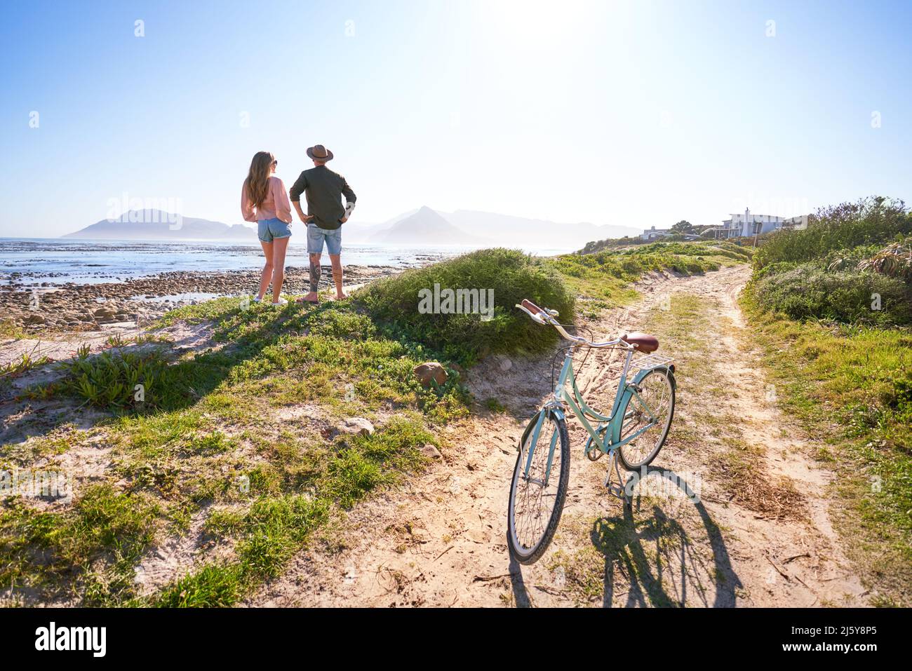 Pärchen, die mit dem Fahrrad am sonnigen, sommerlichen Sandstrand am Ozean stehen Stockfoto