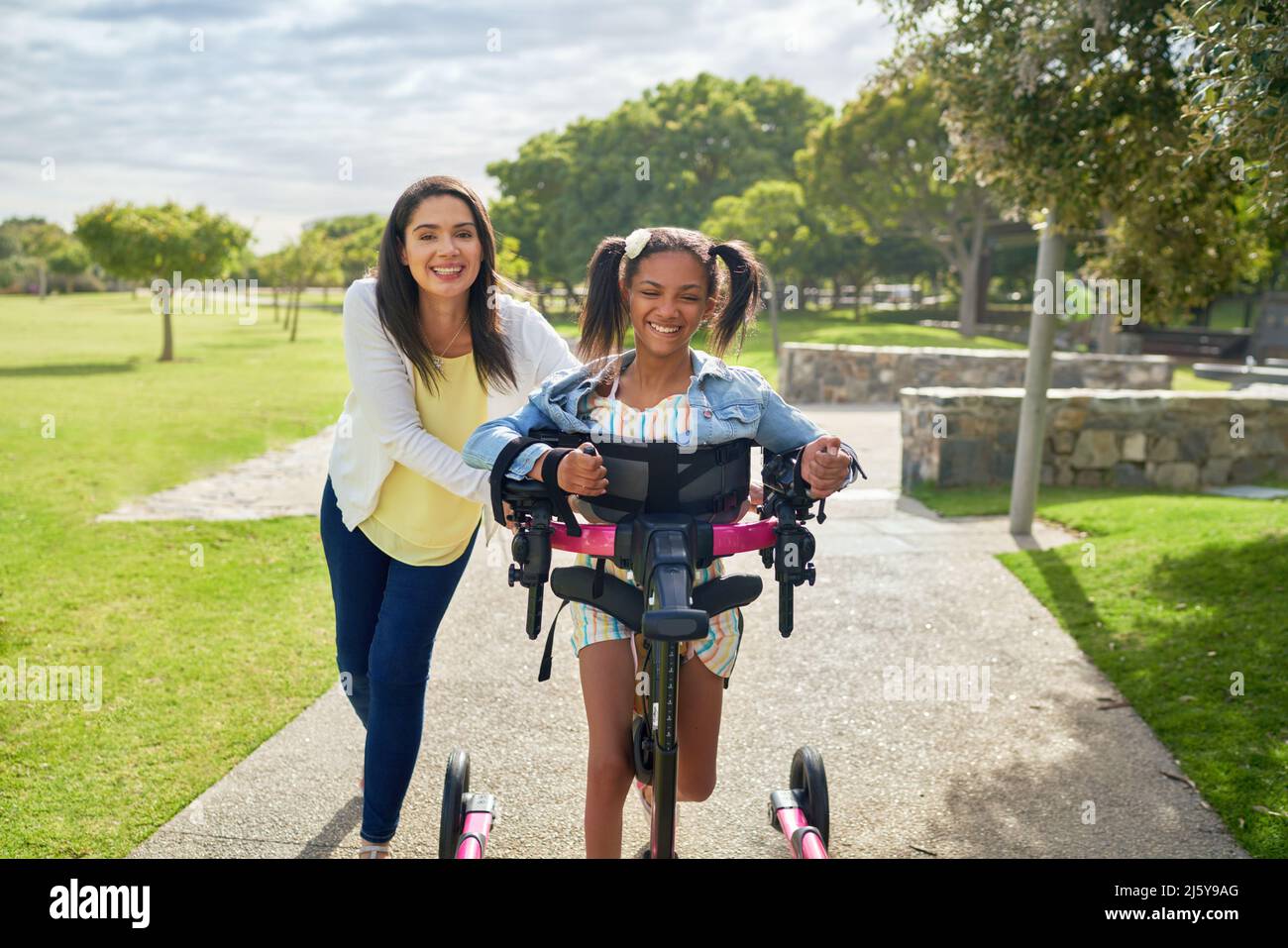 Glückliche Mutter und behinderte Tochter zu Fuß mit Rollator im sonnigen Park Stockfoto