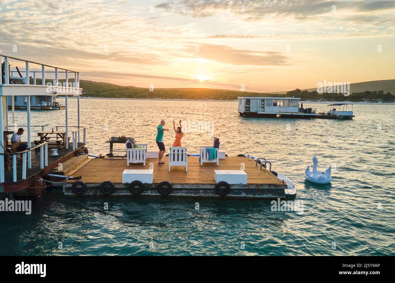 Unbeschwertes Paar, das bei Sonnenuntergang auf der Terrasse des Hausbootes auf dem See tanzt Stockfoto Unbeschwertes Paar, das bei Sonnenuntergang auf der Terrasse des Hausbootes auf dem See tanzt Stockfoto
