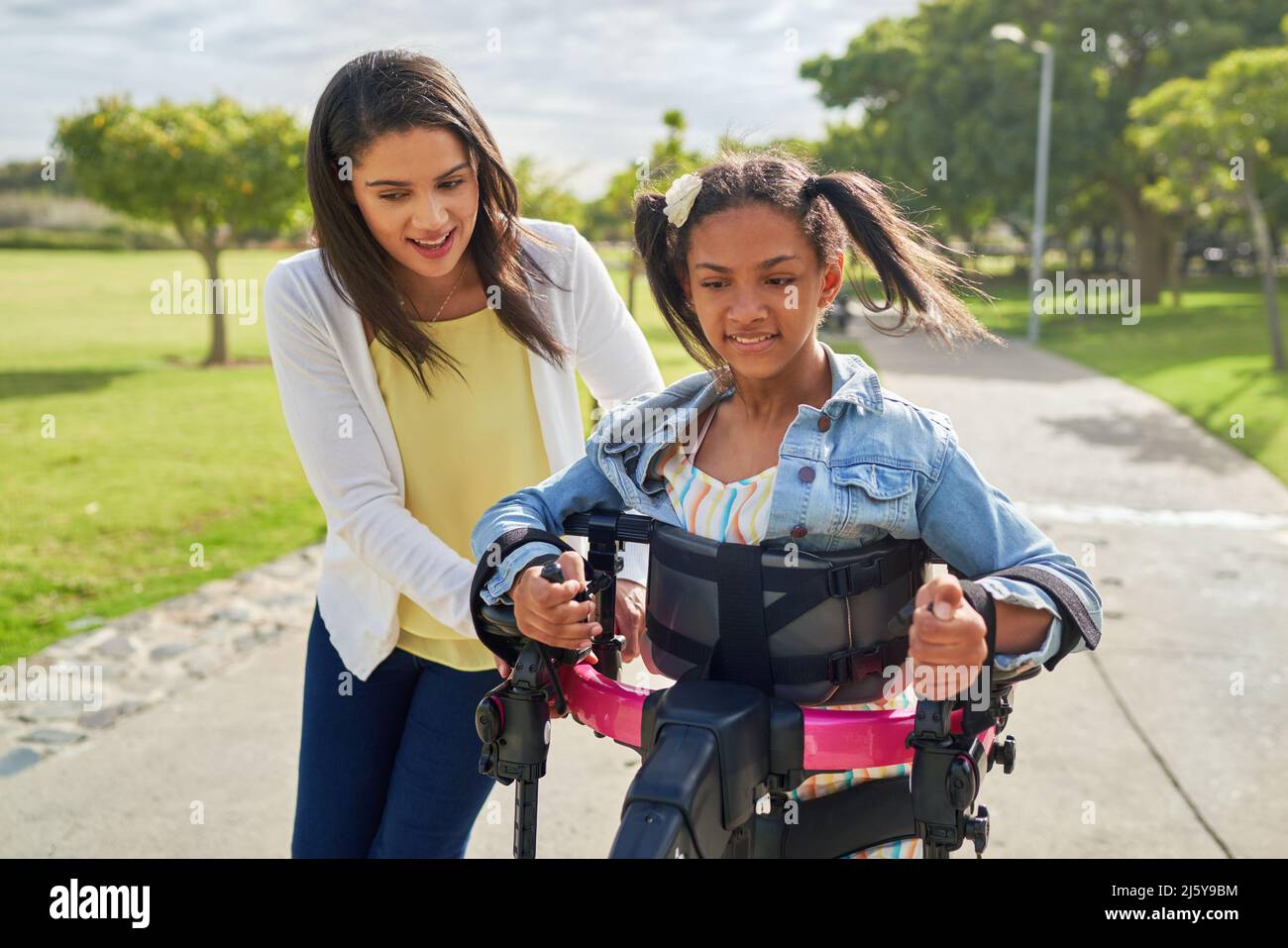 Mutter hilft behinderten Tochter zu Fuß in Rollator im Park Stockfoto