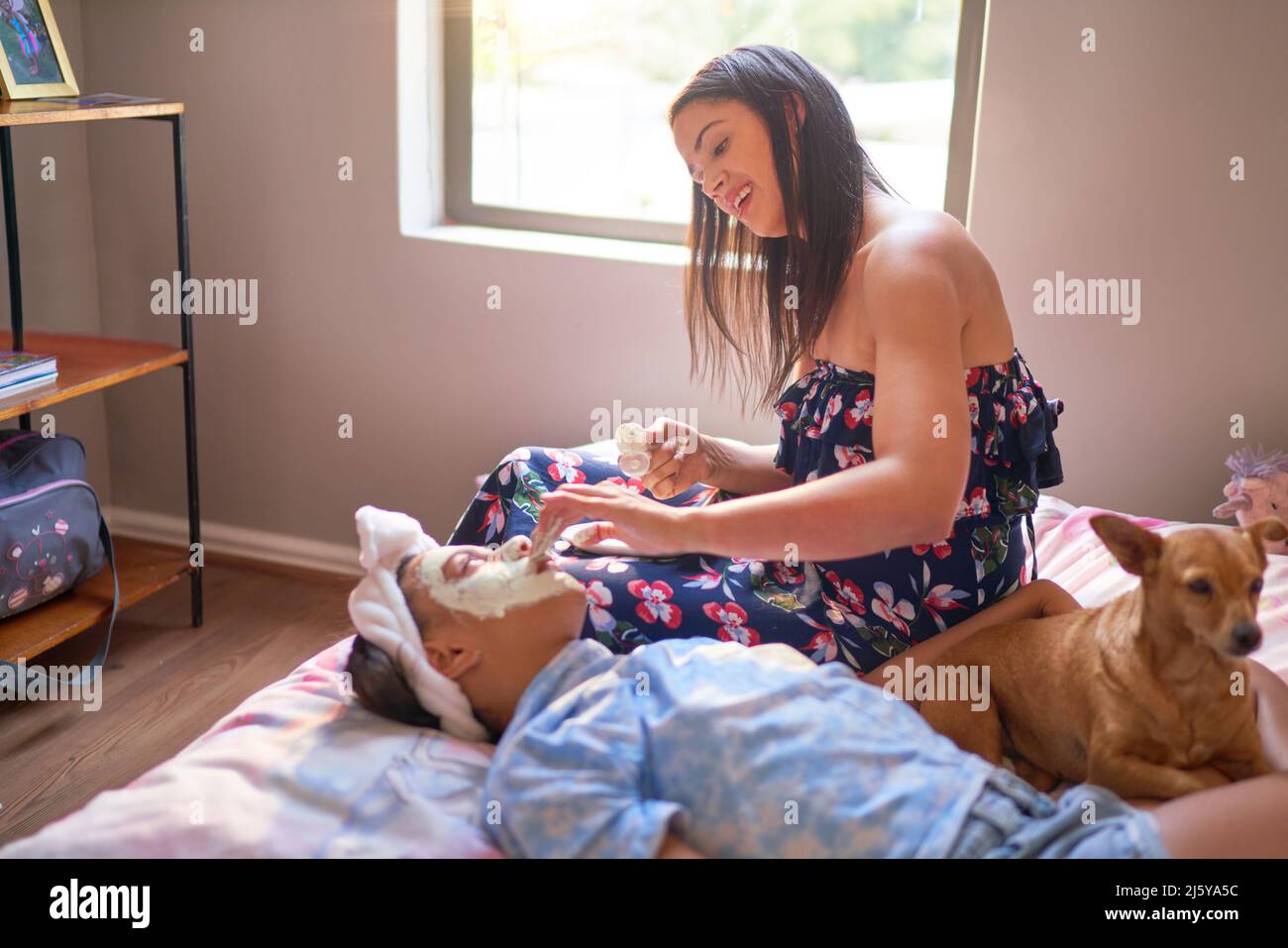 Mutter gibt einer behinderten Tochter zu Hause eine Gesichtsbehandlung auf dem Bett Stockfoto