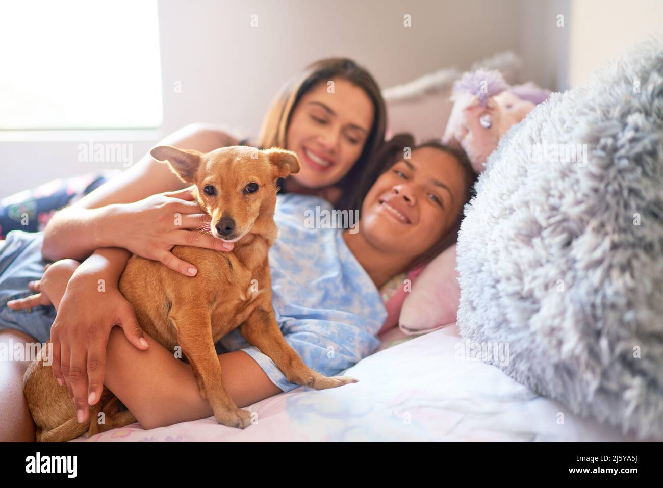 Portrait glückliche Mutter, behinderte Tochter und Hund kuscheln auf dem Bett Stockfoto