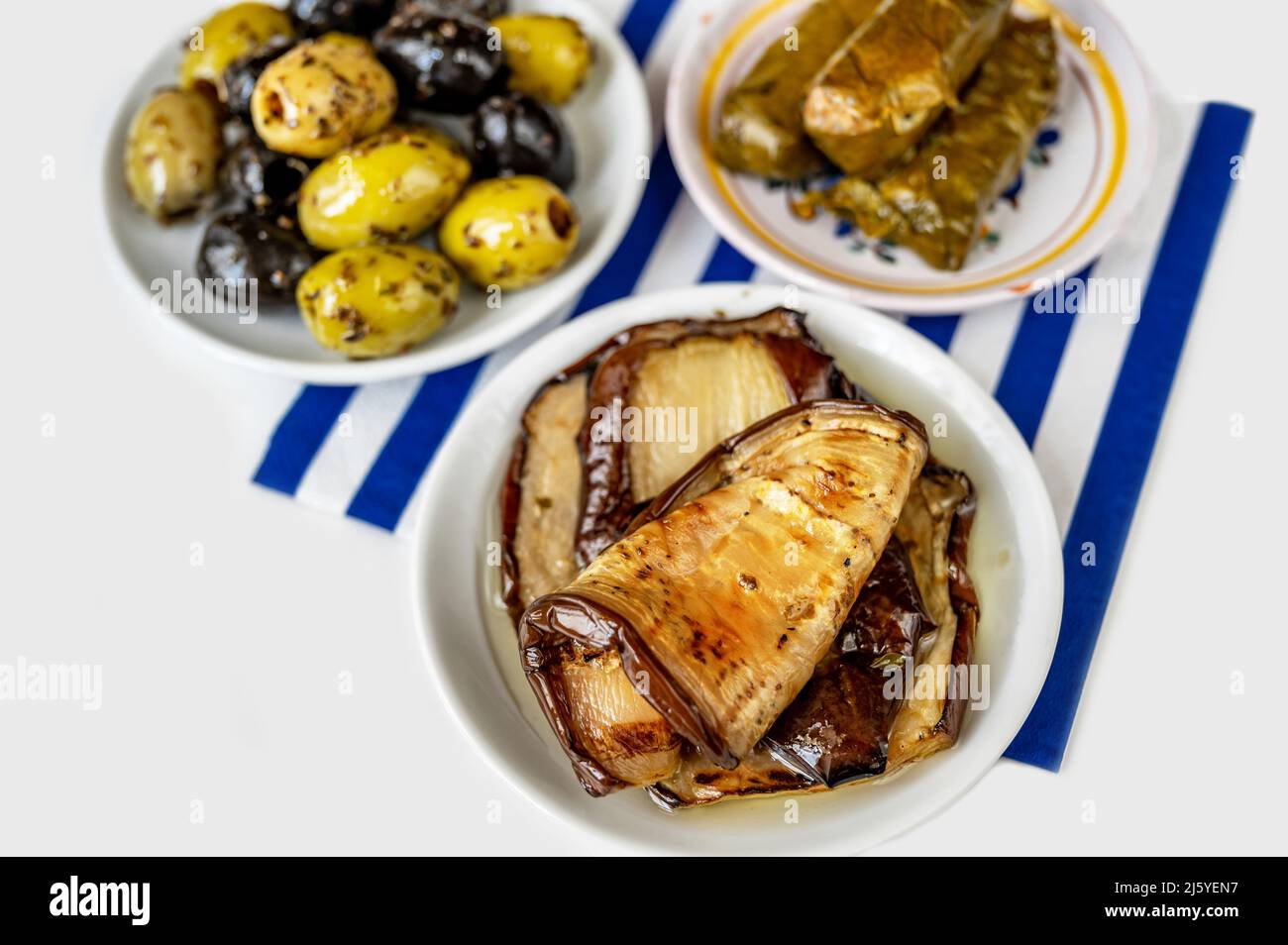 Drei Teller mit Olivenöl in Öl und Kraut, Weinblatt gefüllt mit Reis (Dolmades) und geschnittene Auberginen auf blau gestreiftem Handtuch. Griechische und mediterrane Ausstattung Stockfoto