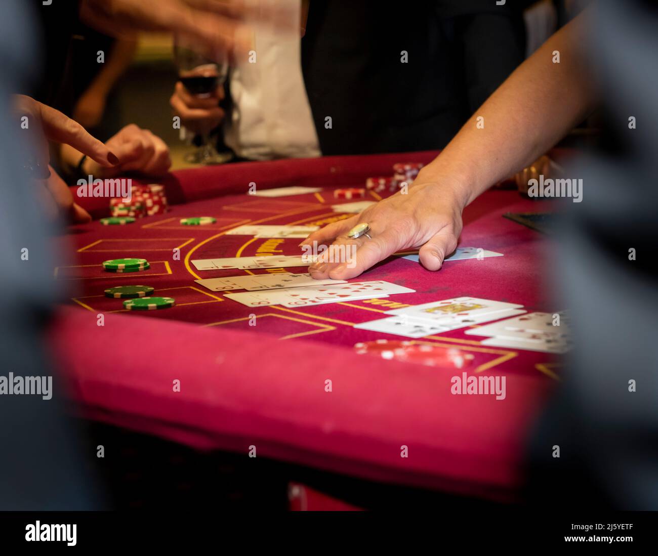 Kaukasische weibliche Hand, die Karten auf einem runden roten Casino-Tisch ausgibt. Stockfoto