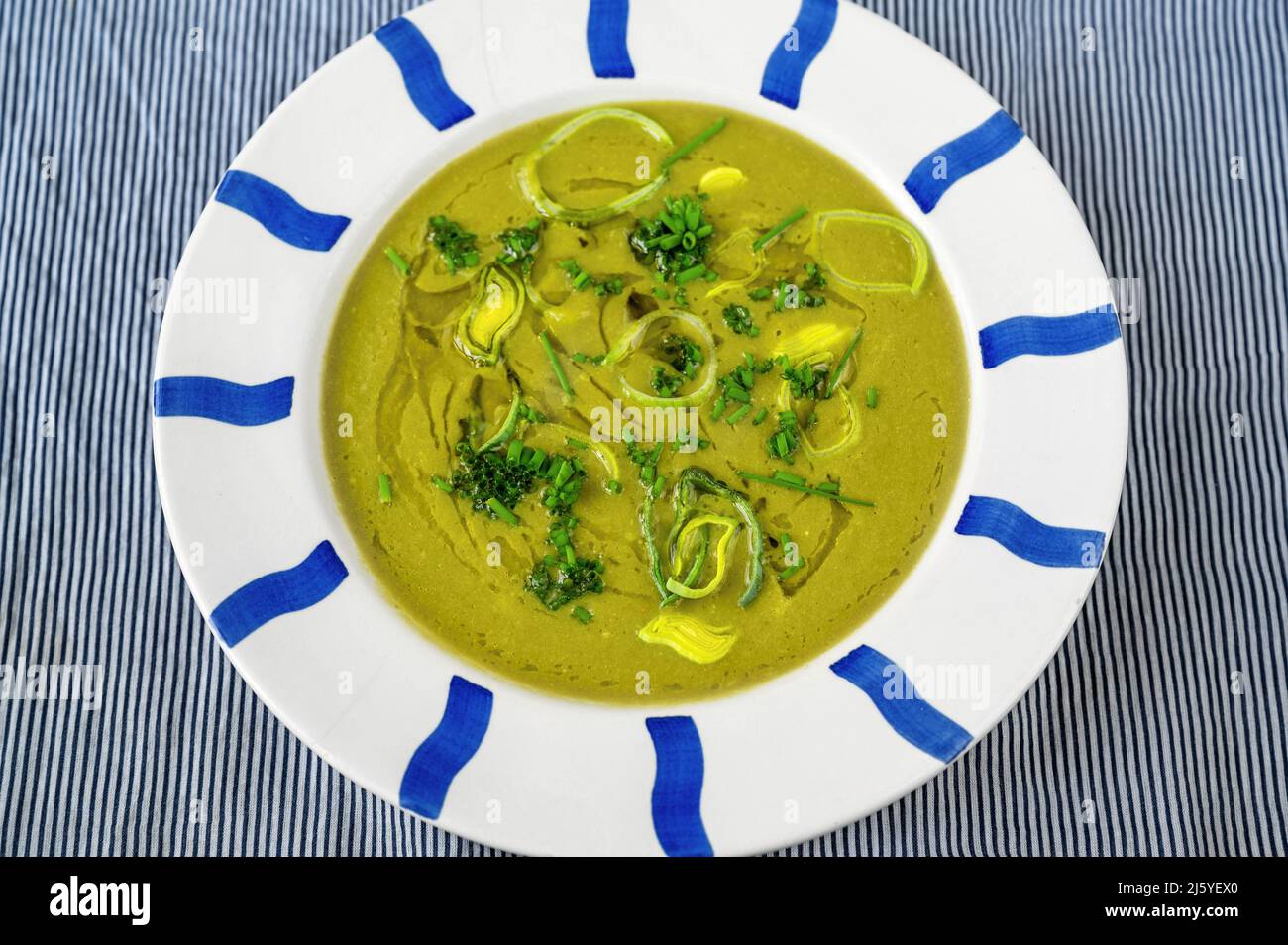 Lauch-Suppe in blau gestreiftem Teller auf blauem Tisch, Nahaufnahme. Stockfoto