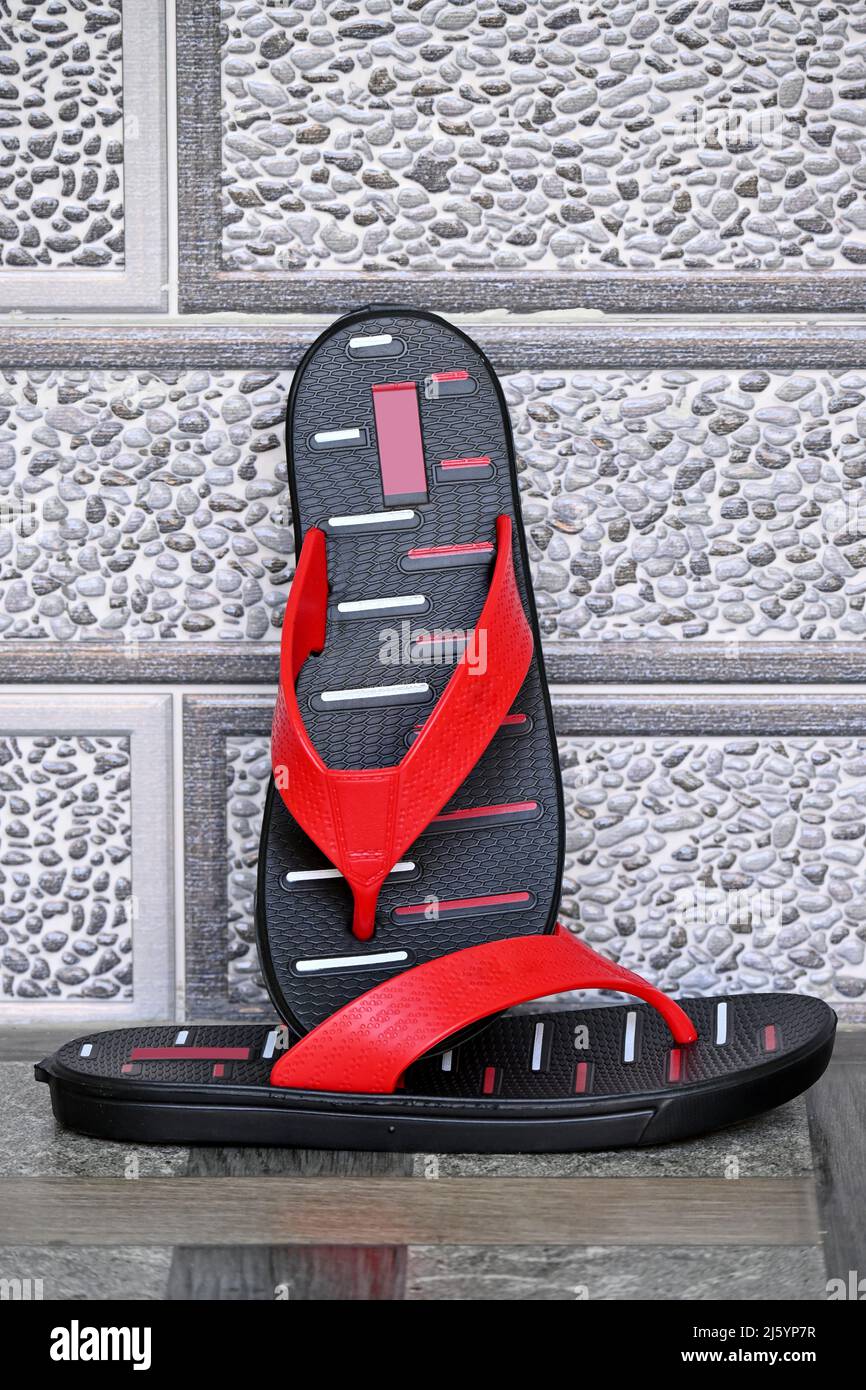 Nahaufnahme des roten schwarzen Slippers auf unscharfem graubraunen Hintergrund. Stockfoto