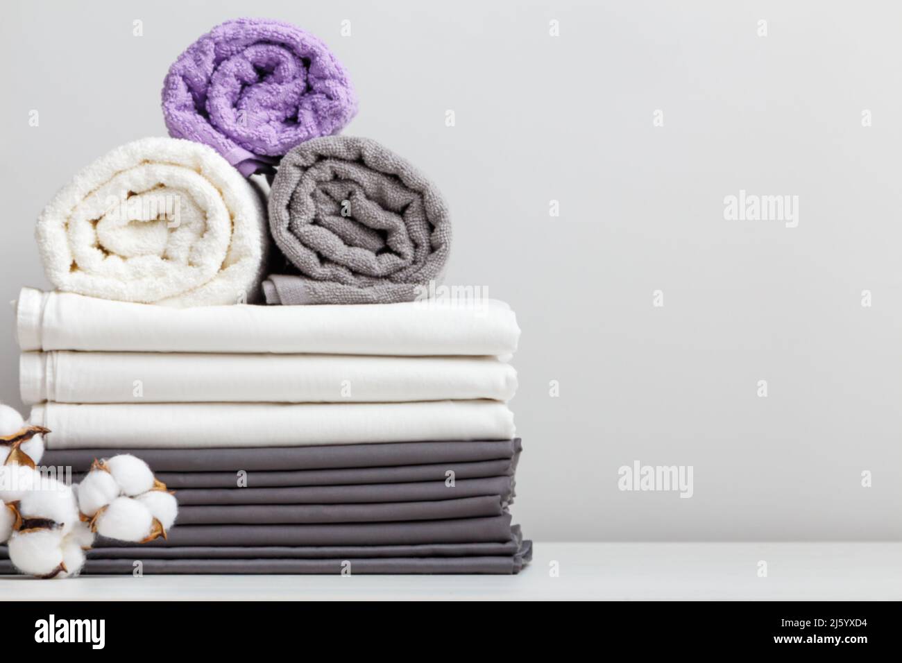 Stapel von Bettwäsche, Bettwäsche und Handtücher mit Baumwollzweig auf dem Tisch Kopieplatz Stockfoto