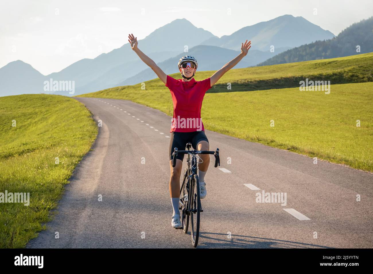 Glückliche Radrennfahrerin in Freude, mit über dem Kopf erhobenen Armen, nachdem sie erfolgreich ein Ziel erreicht hatte Stockfoto
