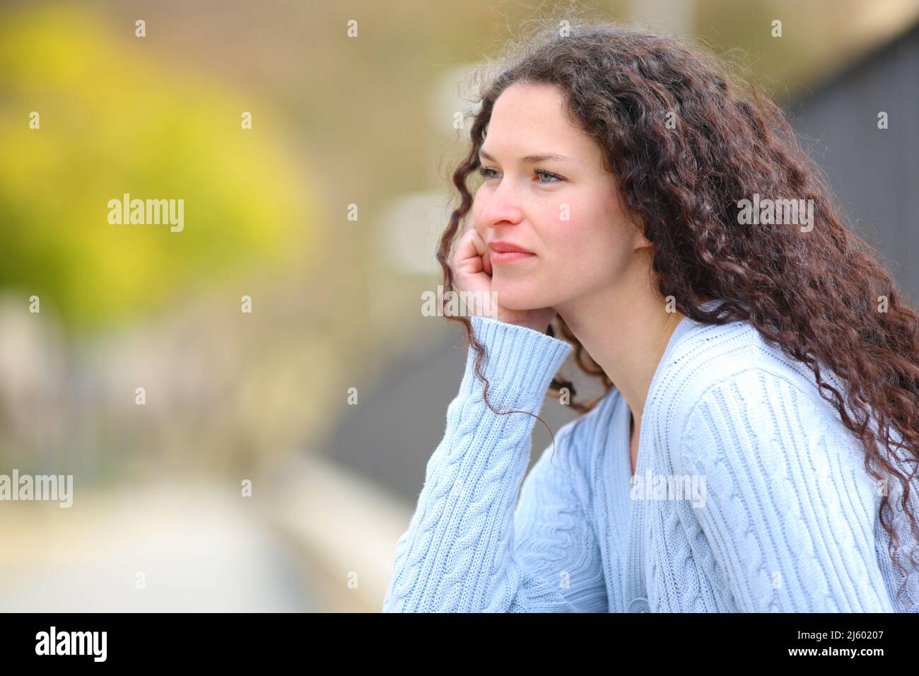 Seriöse, nachdenkliche Frau, die in einem Park sitzt und wegschaut Stockfoto