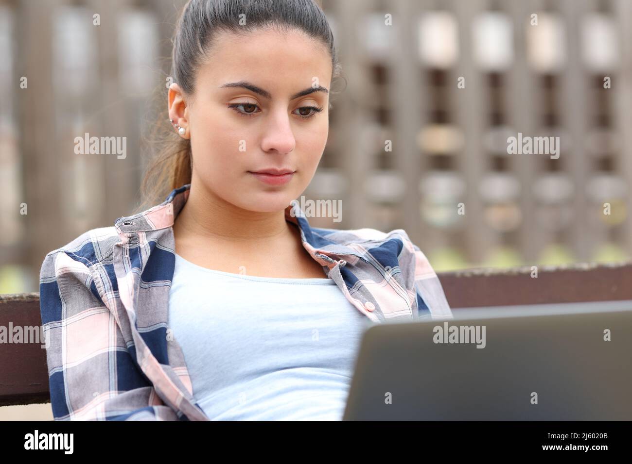 Teen prüft Laptop-Inhalte auf einer Bank in einem Park sitzen Stockfoto