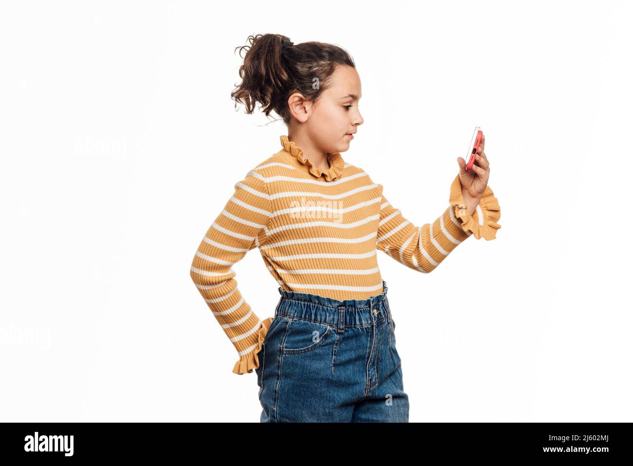 Mädchen, die ein Mobiltelefon benutzt, während sie auf einem isolierten weißen Hintergrund steht. Stockfoto