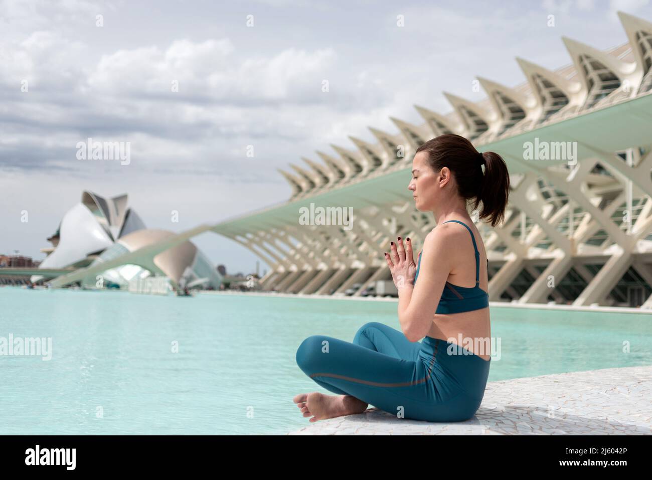 Frau praktiziert Yoga am Wasser in der Stadt der Künste und Wissenschaften, Valencia, Spanien. Stockfoto