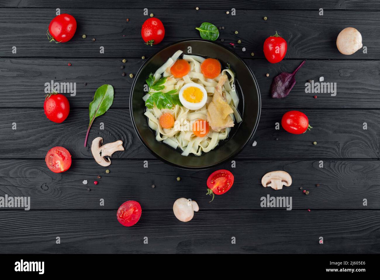 Bouillon mit Nudeln mit Gemüse auf schwarzem Strukturhintergrund mit Huhn. Stockfoto