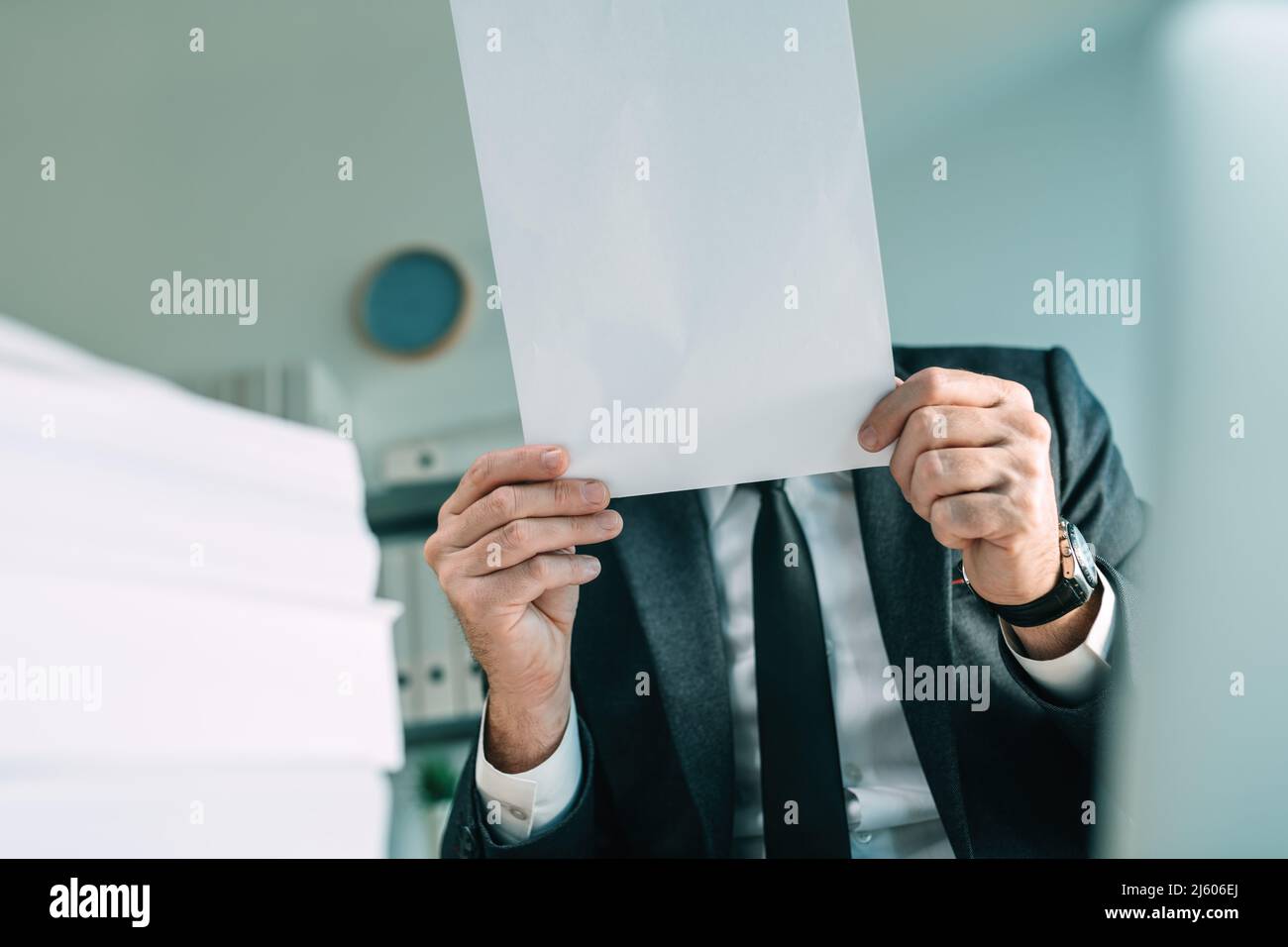 Nicht erkennbarer Geschäftsperson, der weißes Mockup-Papier vor seinem Gesicht als Kopierfläche hält, selektiver Fokus Stockfoto