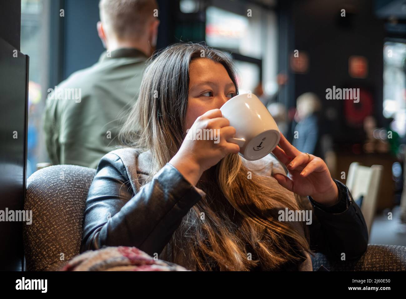 Lange Haare Hispanic junge Erwachsene männlich trinken in einem Becher im Hipster Coffee Shop Stockfoto