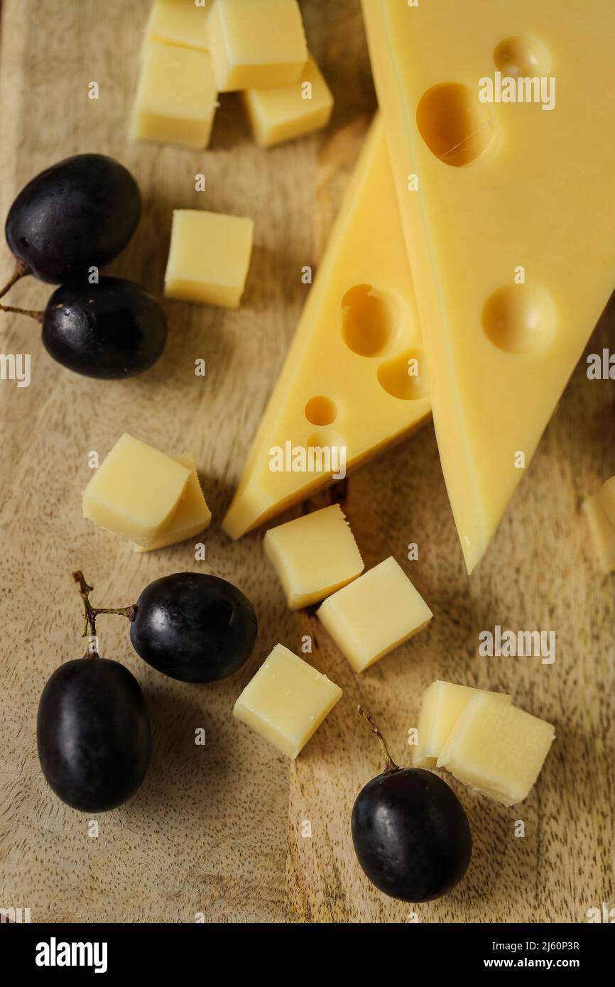 Käse mit Früchten geschnitten.Mazdar Käse Dreiecke, gouda Käse Würfel und schwarze Trauben.Käse mit Trauben auf Holzbrett Hintergrund Stockfoto