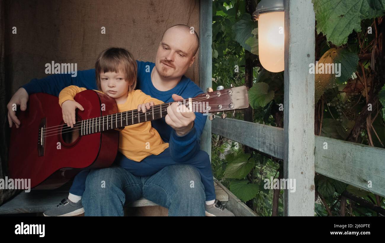 Papa spielt für sein kleines Kind eine akustische Gitarre. Altes Retro-Dekor Stockfoto