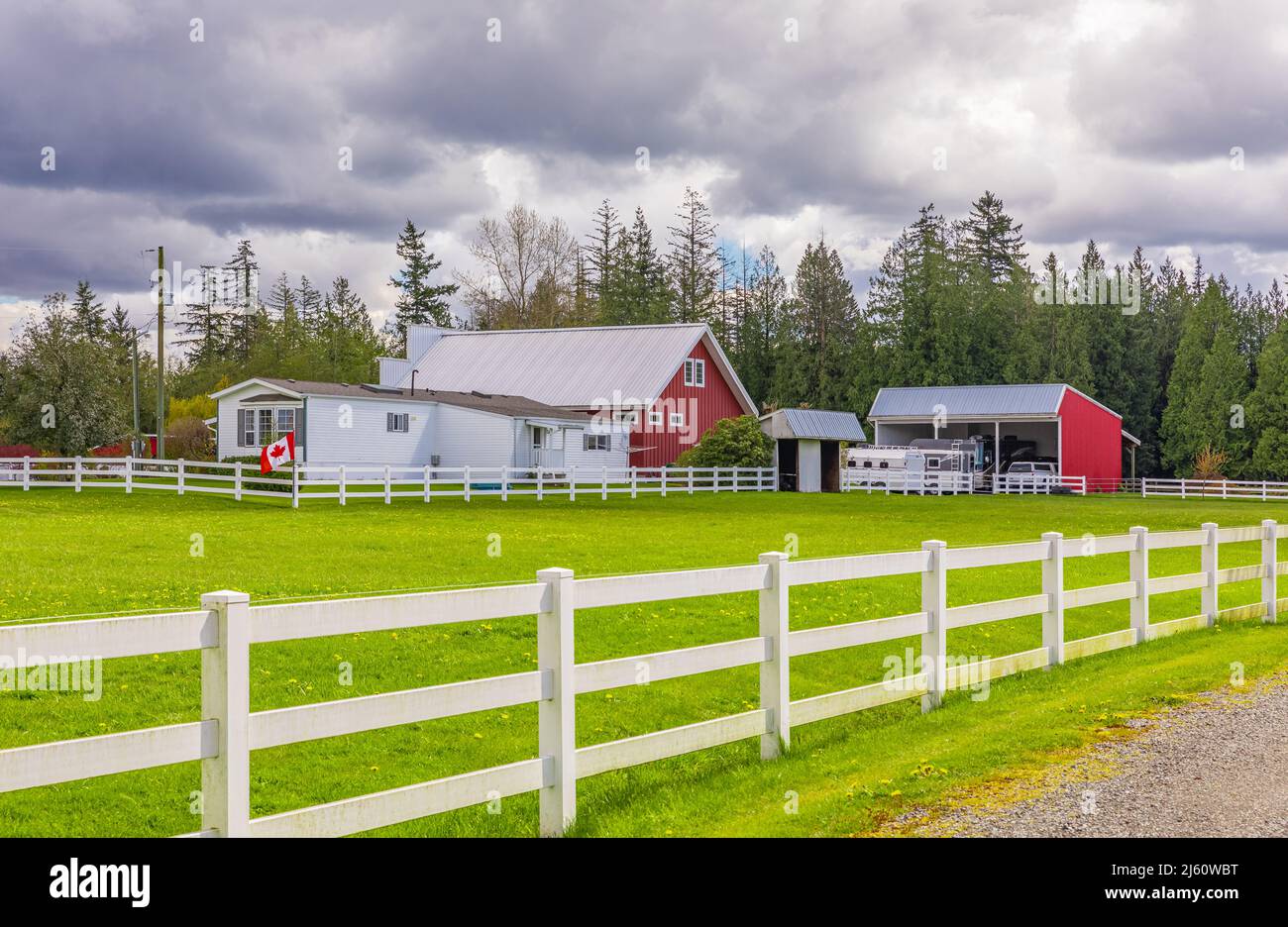 Typisches nordamerikanisches Country Farm House mit weißem Zaun an bewölktem Tag. Hof mit dem Haus und der roten Scheune. Reisefoto, selektiver Fokus, Nobo Stockfoto