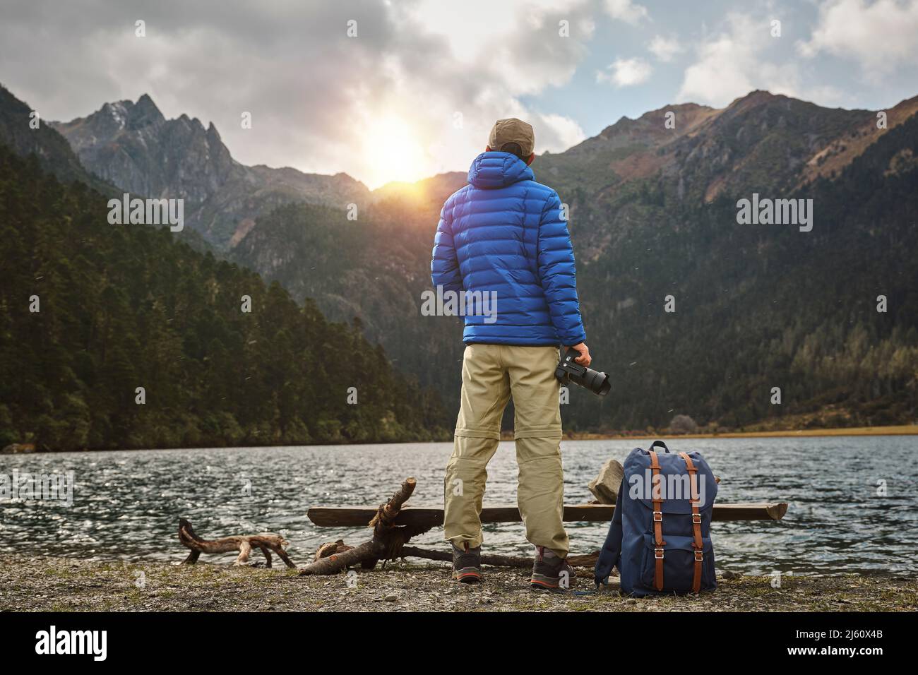 Rückansicht des asiatischen Fotografen, der den Sonnenuntergang über den Bergen betrachtet Stockfoto