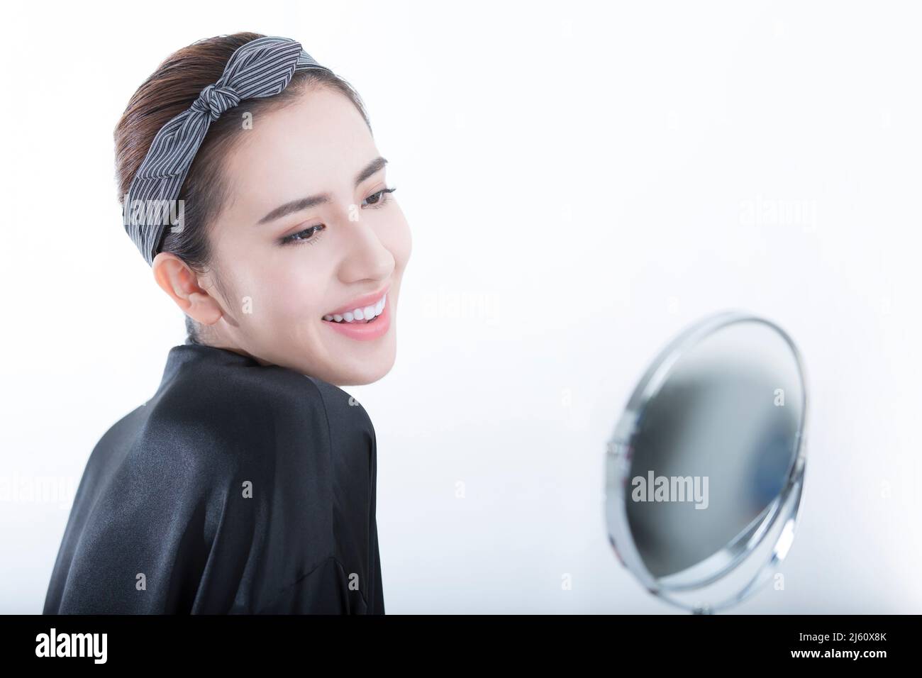 Eine elegante junge chinesische Frau, die ihr zartes Make-up in einem Spiegel auf weißem Hintergrund betrachtet - Stock Foto Stockfoto