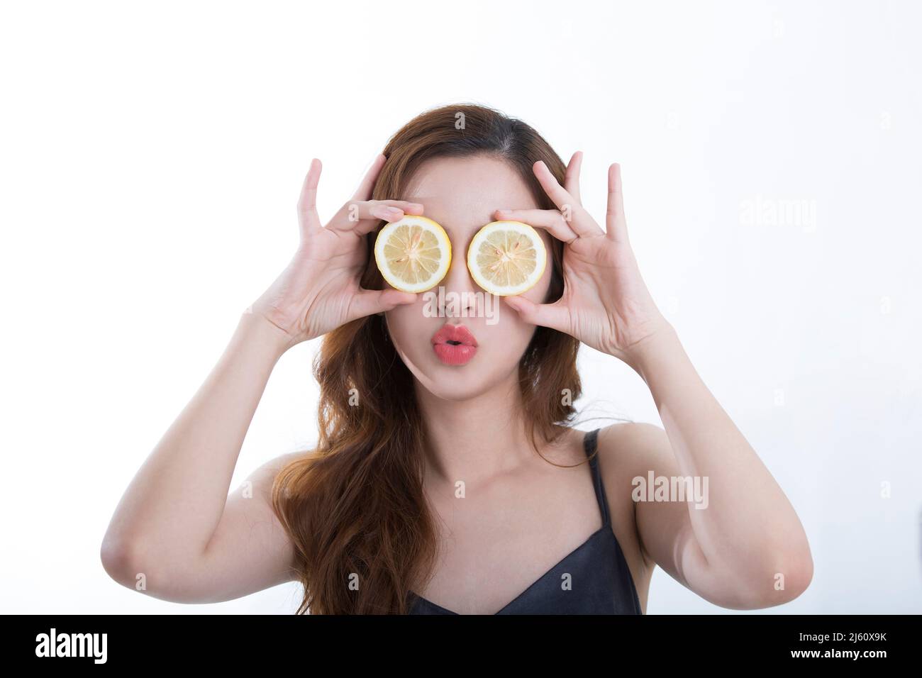 Hübsche junge Dame bedeckte ihre Augen spielerisch mit einer Zitronenscheibe, auf weißem Hintergrund - Stockfoto Stockfoto