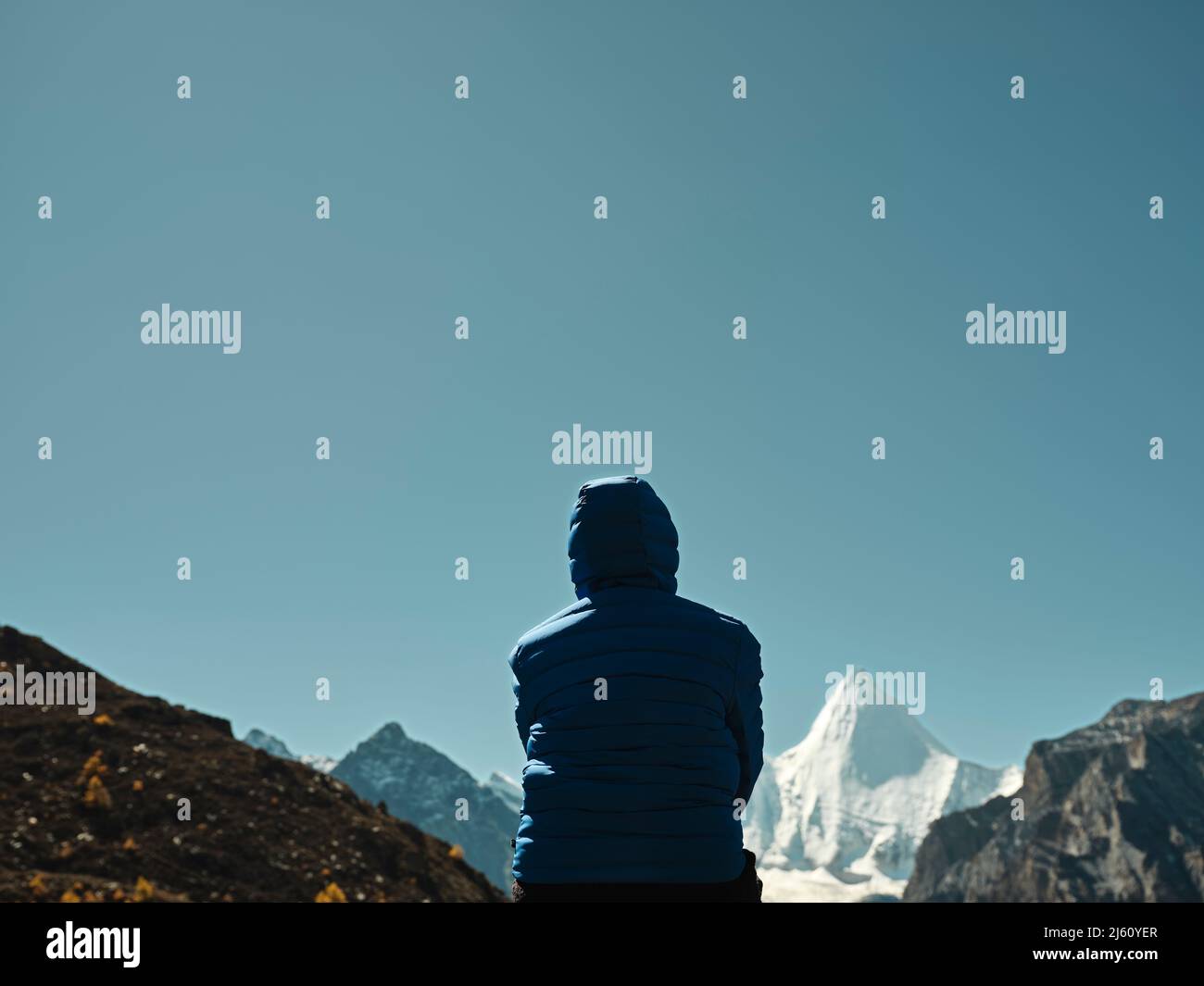 Rückansicht einer asiatischen Frau, die auf einem nahe gelegenen Berg sitzt und den Berg Yangmaiyong (oder Jampayang auf Tibetisch) in Yading, Kreis Daocheng, Sichua, anschaut Stockfoto