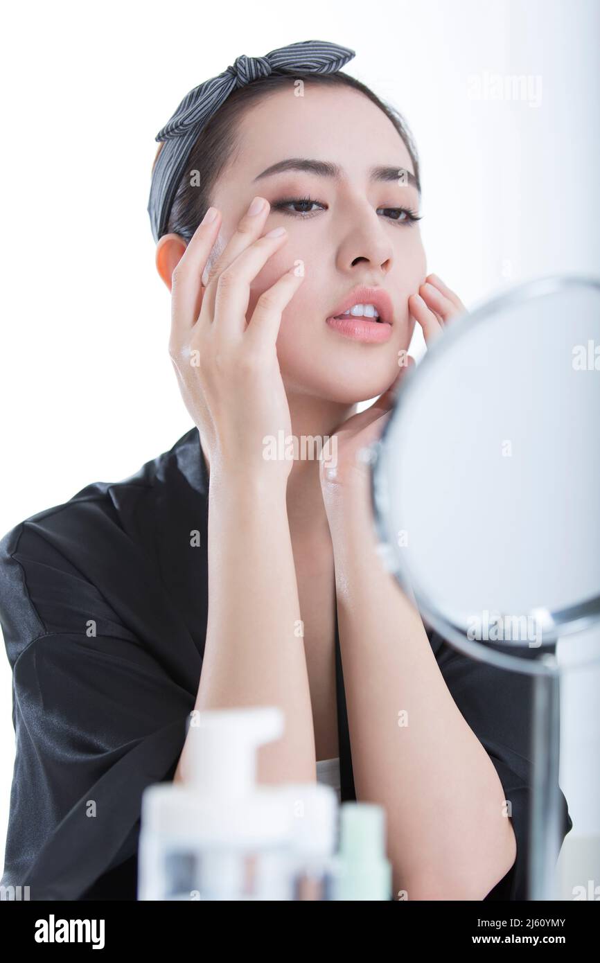 Schöne junge chinesische Frau mit Hautpflegeprodukten vor einem Kosmetikspiegel, auf weißem Hintergrund - Stock Foto Stockfoto