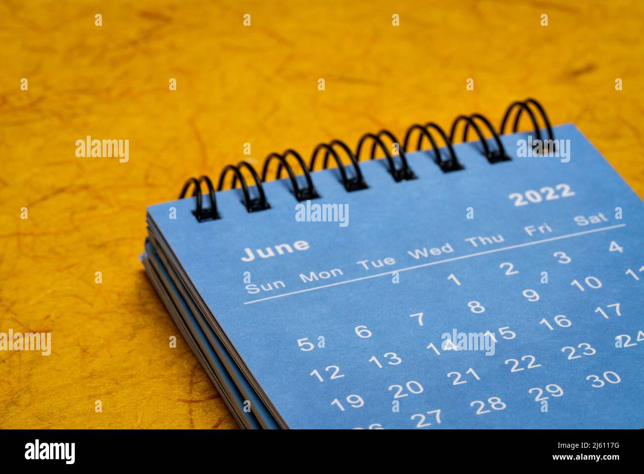 Juni 2022 - blauer Spiral-Desktop-Kalender gegen knallorangefarbenes handgemachtes Papier, Zeit- und Geschäftskonzept Stockfoto