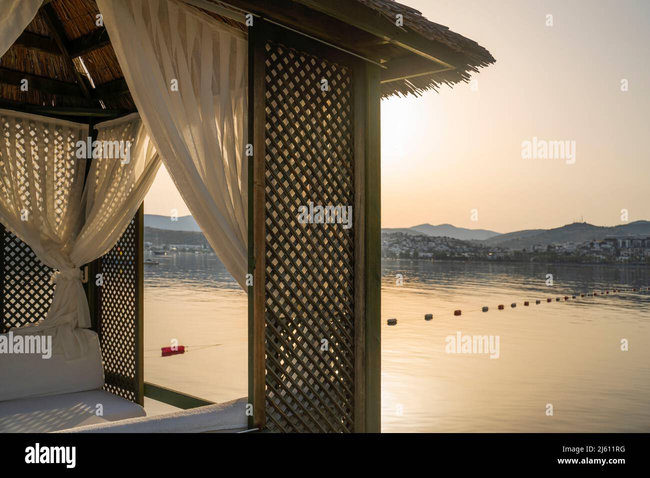 Romantischer Pavillon an einem tropischen Strand. Sommermorgendliche Landschaft mit Strohpavillon mit weißen Vorhängen Stockfoto