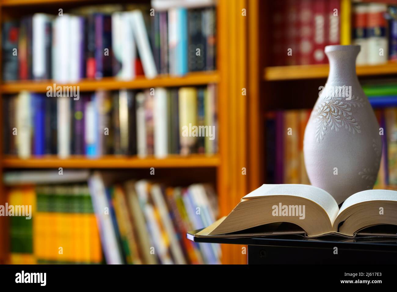 Bibliothek mit vielen Büchern zum Lesen, auf Regalen angeordnet. Öffnen Sie Buch und Vase im Vordergrund. Speicherplatz kopieren. Hintergrund. Stockfoto