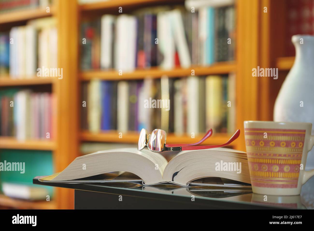 Bibliothek mit vielen Büchern zum Lesen, auf Regalen angeordnet. Öffnen Sie Buch, Gläser und Tasse Nahaufnahme. Speicherplatz kopieren. Hintergrund. Stockfoto