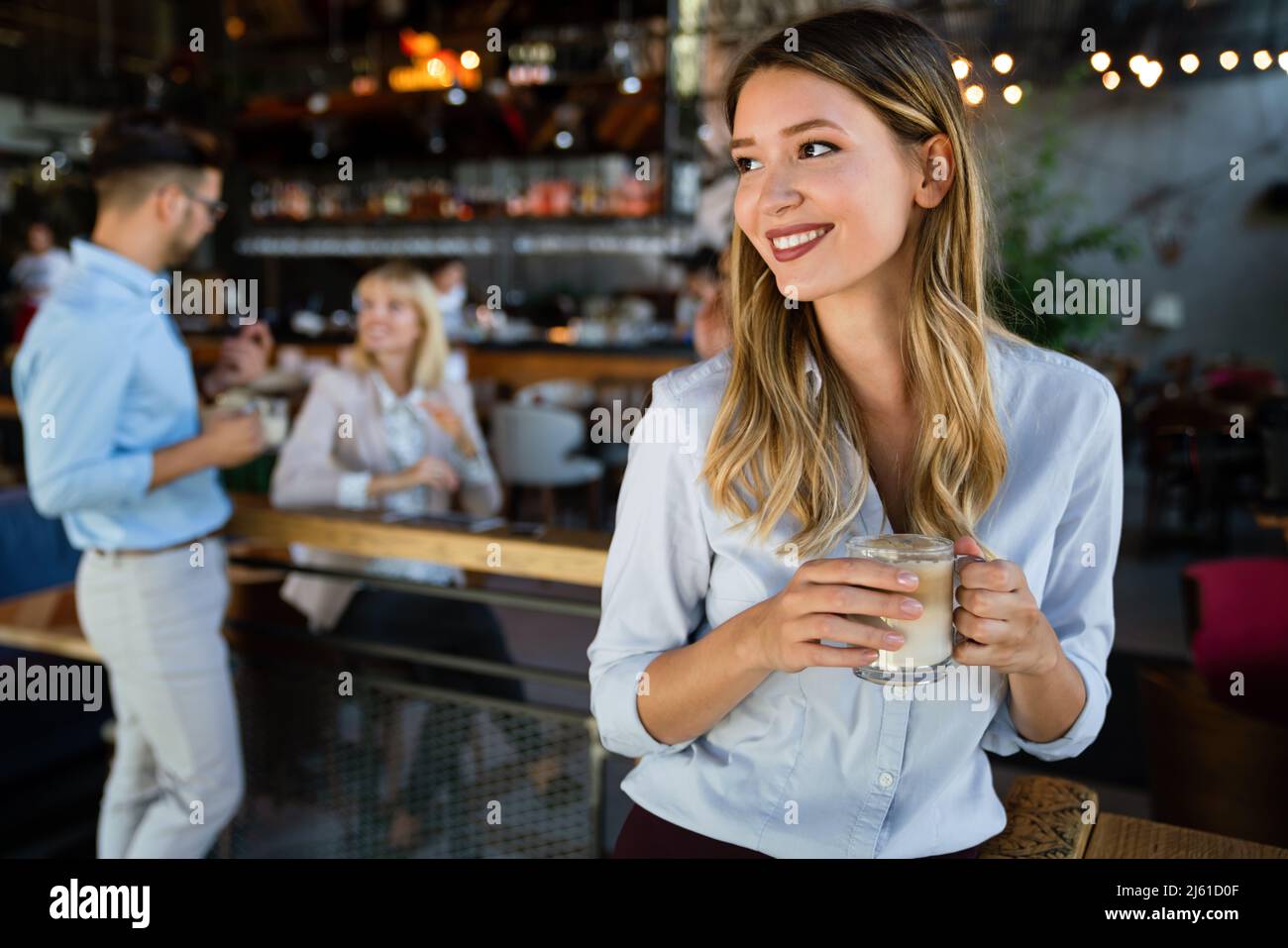 Porträt einer glücklichen jungen Geschäftsfrau, die in einer Pause Kaffee trinkt. Im Hintergrund ihre Kollegen Stockfoto