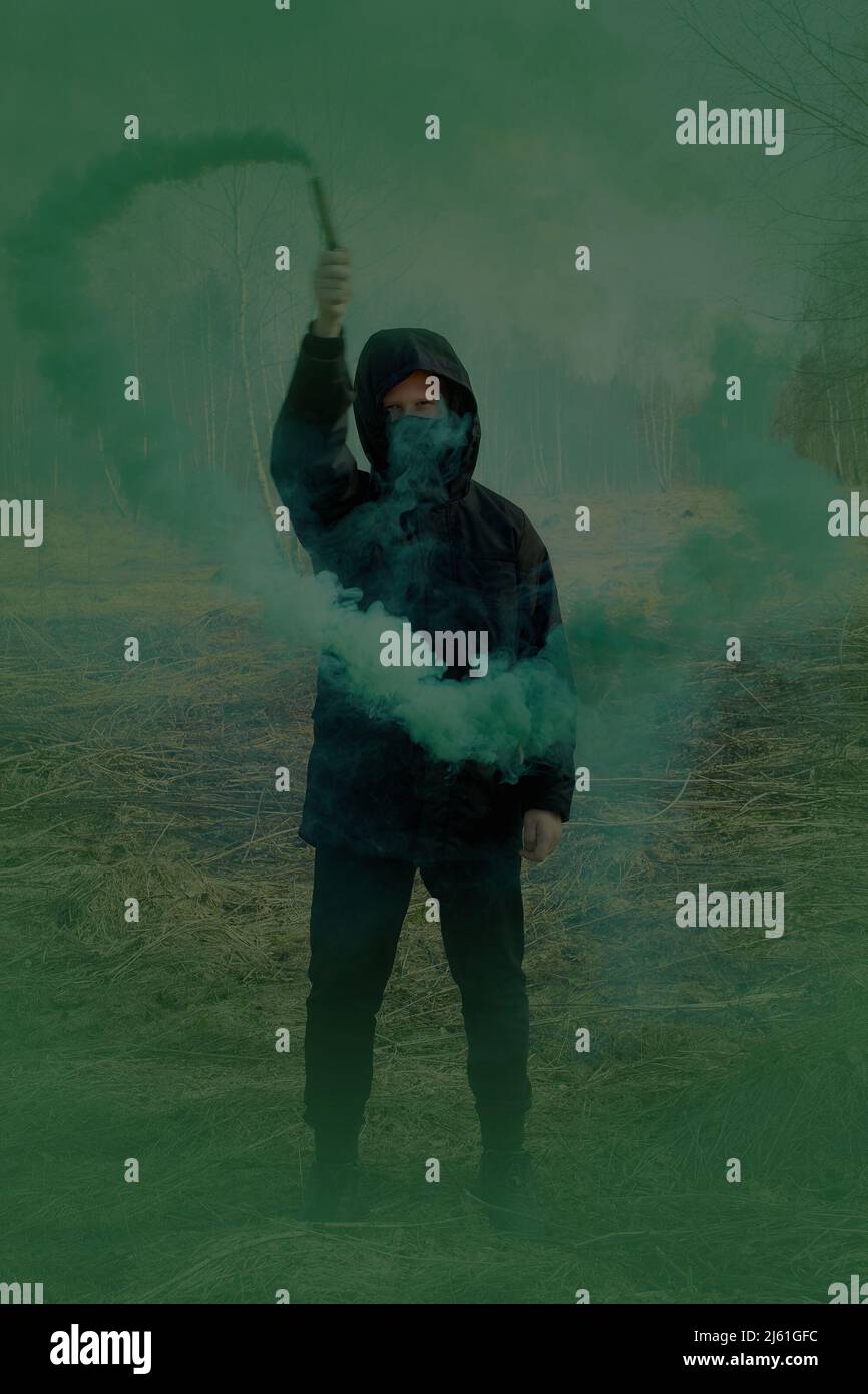 Ein Teenager in einer schwarzen Jacke und einer Maske hält eine grüne Rauchbombe Stockfoto