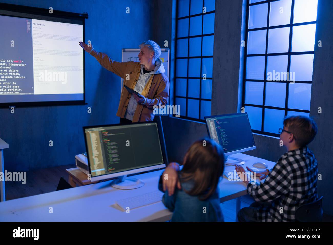 Lehrer, der jungen Studenten im dunklen Raum einen Informatikvortrag hält. Zimmer. Erläuterung Der Informationstechnologie. Stockfoto